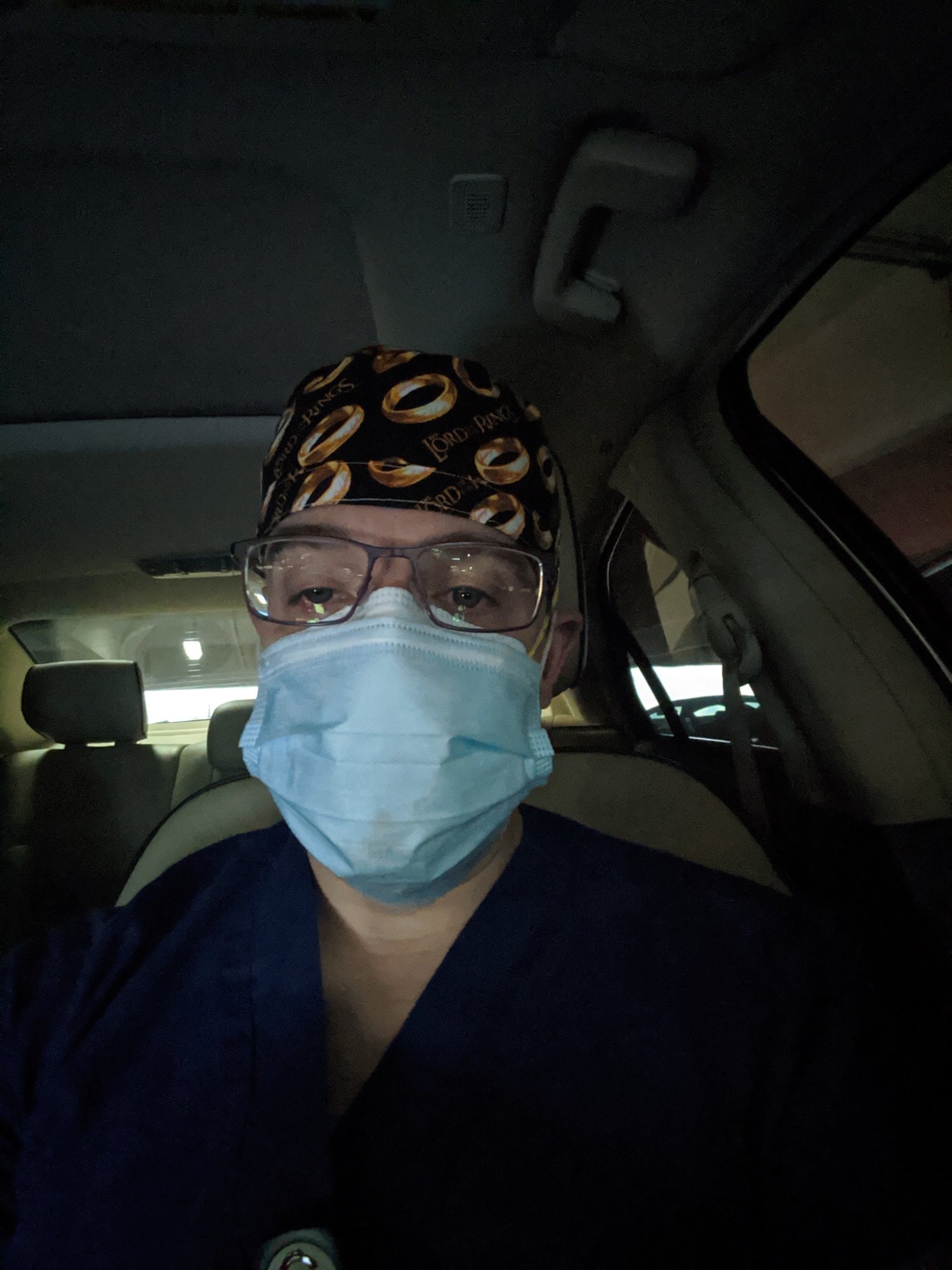 Travis in scrubs, a surgical mask and a scrub cap, sitting in his car early in the morning