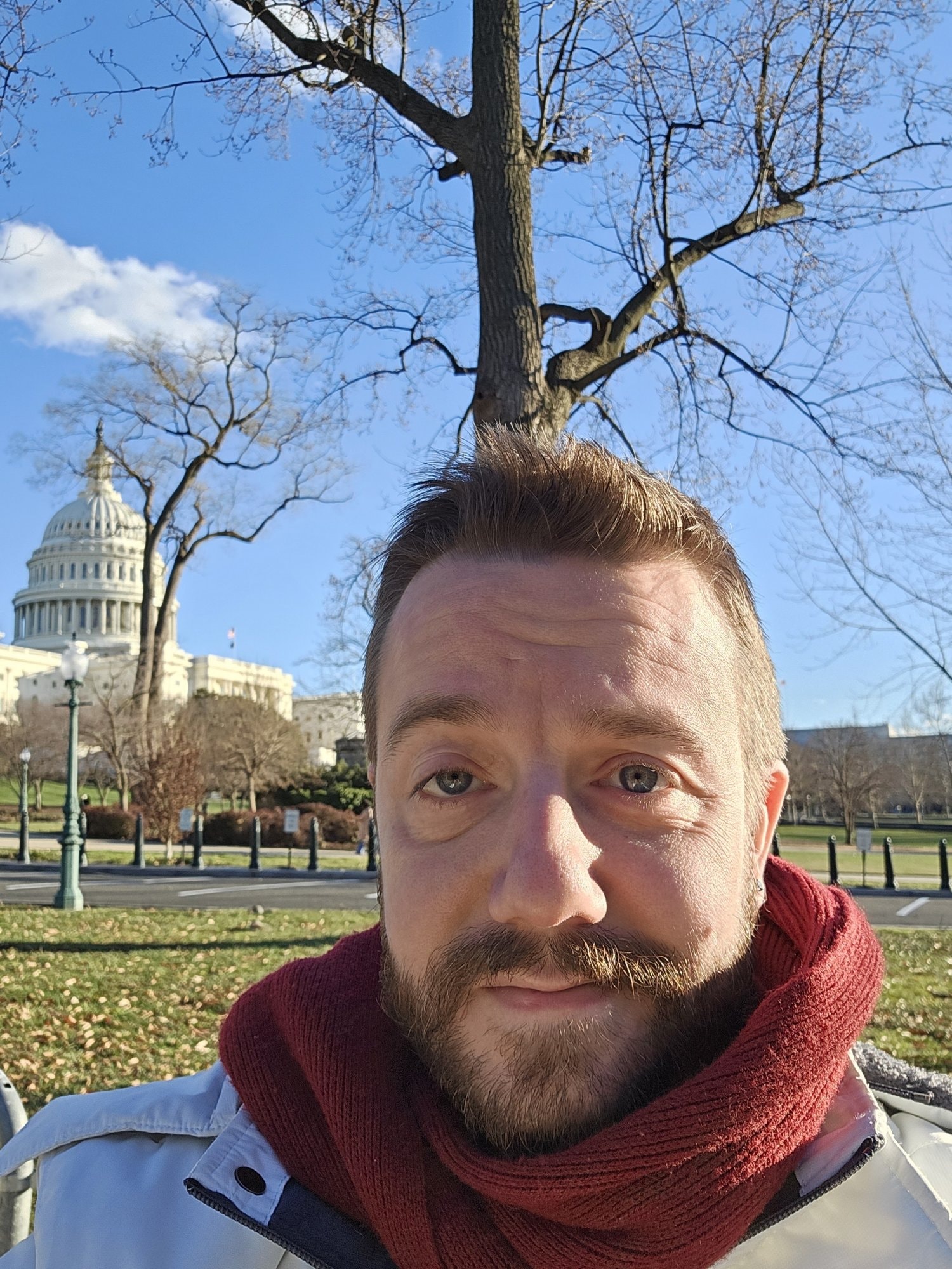 Travis in a red scarf in front of the U.S. Capitol dome on a clear winter day